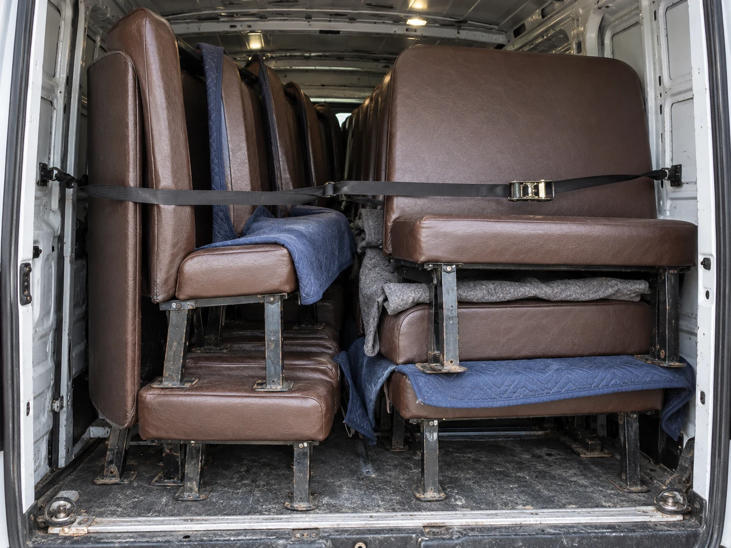 School bus bench seats stacked and strapped in a work van