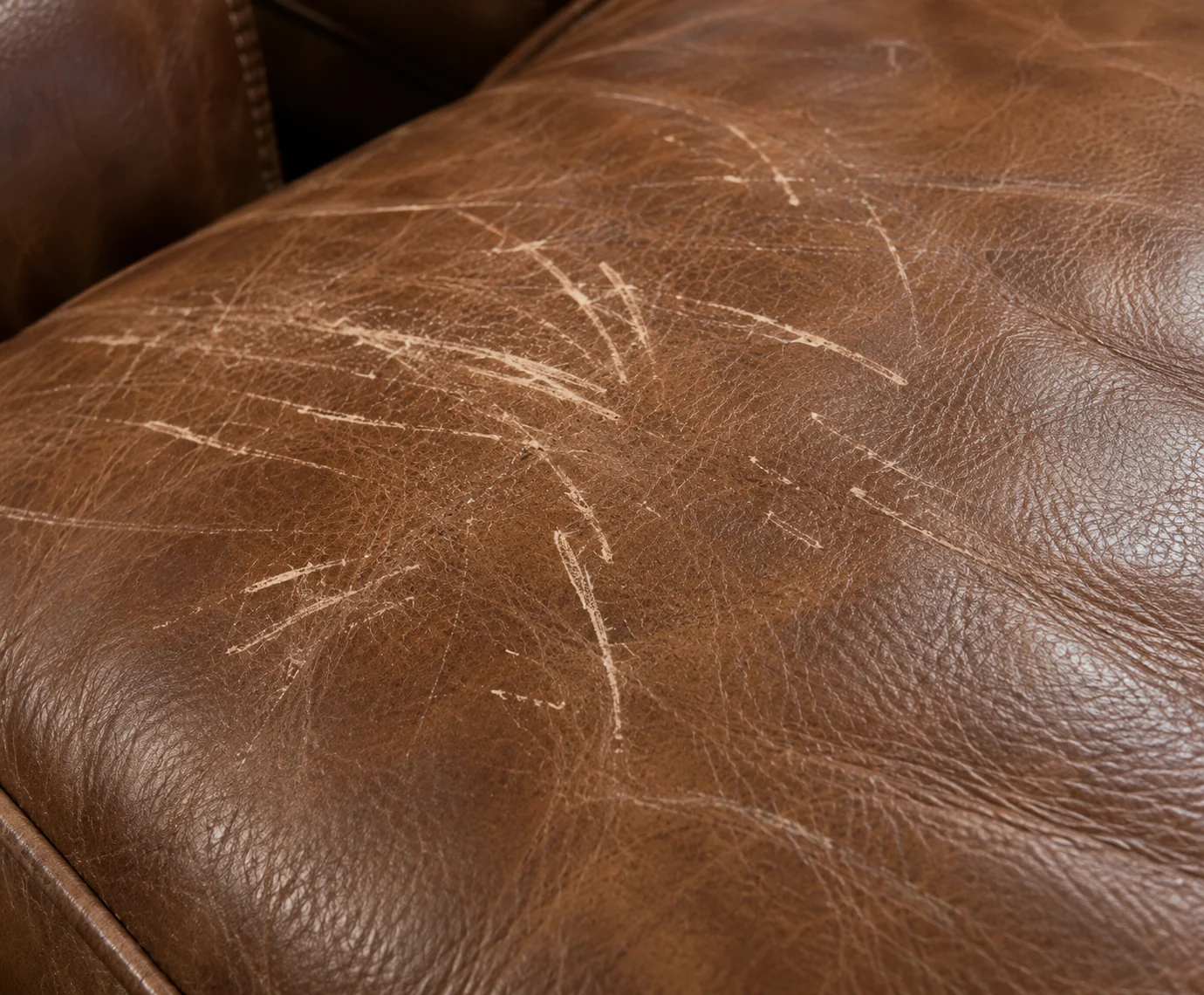Pale scratch marks scored across the top of a brown leather ottoman