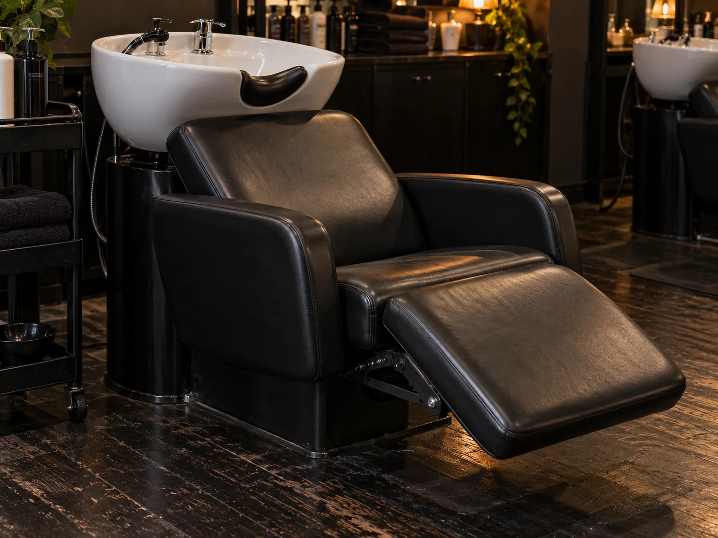 A black shampoo chair seat and leg rest beside its backwash basin