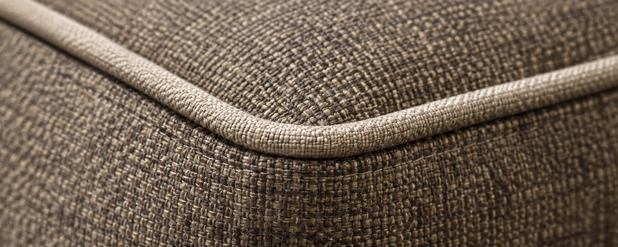 A woven upholstery corner with a pale contrast welt running over it