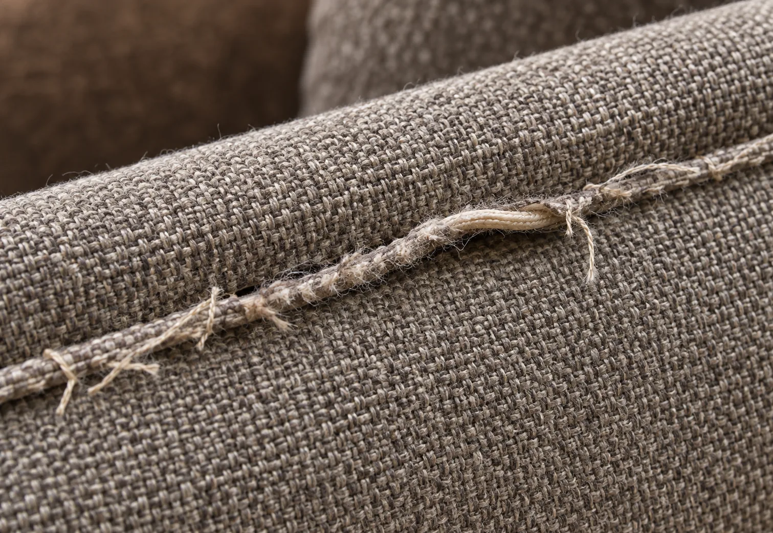 A burst upholstery seam with the stitching open and threads frayed