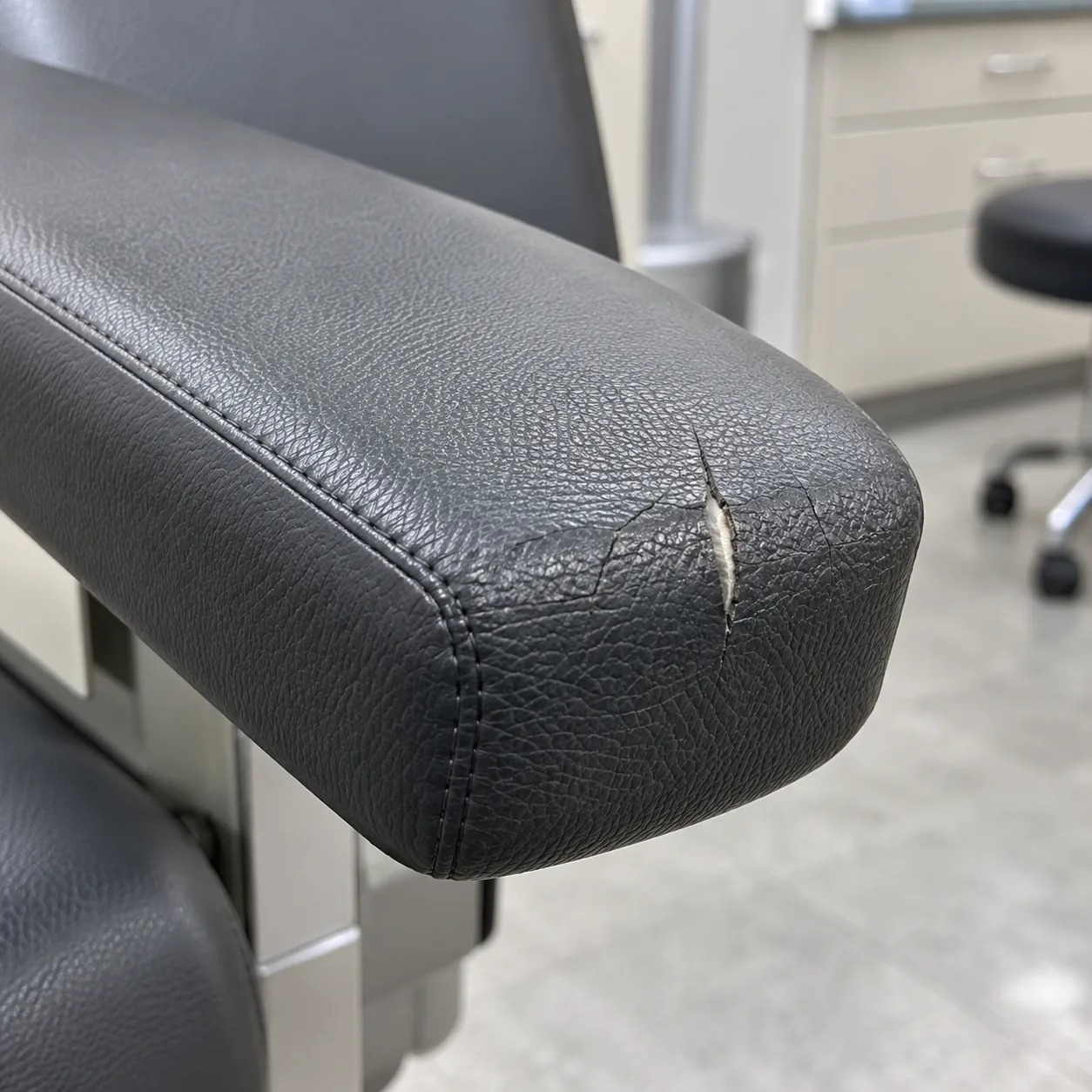 A split in the charcoal vinyl at the end of a medical chair armrest