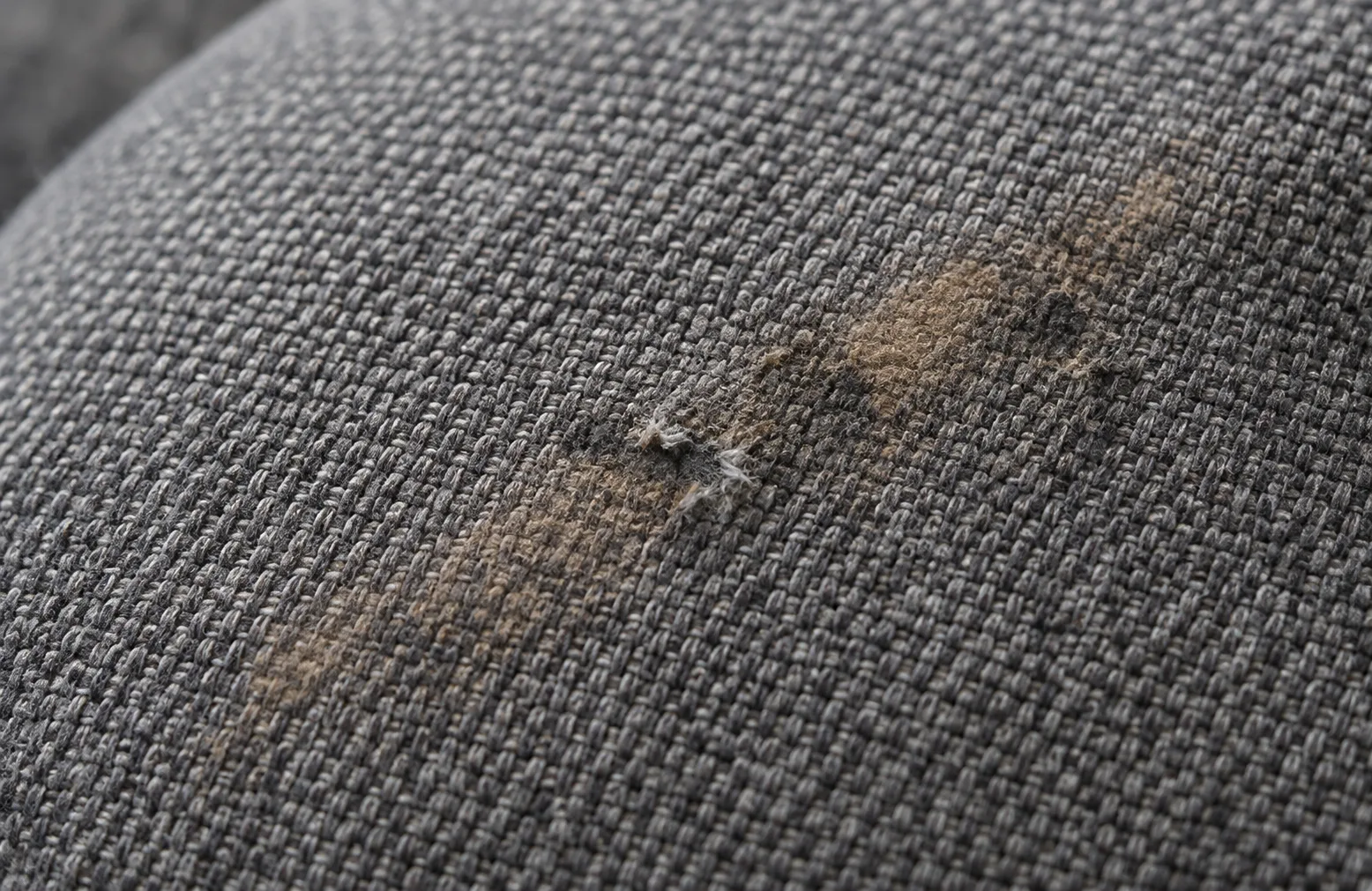 Grey chair fabric with a stain and a small tear in the weave