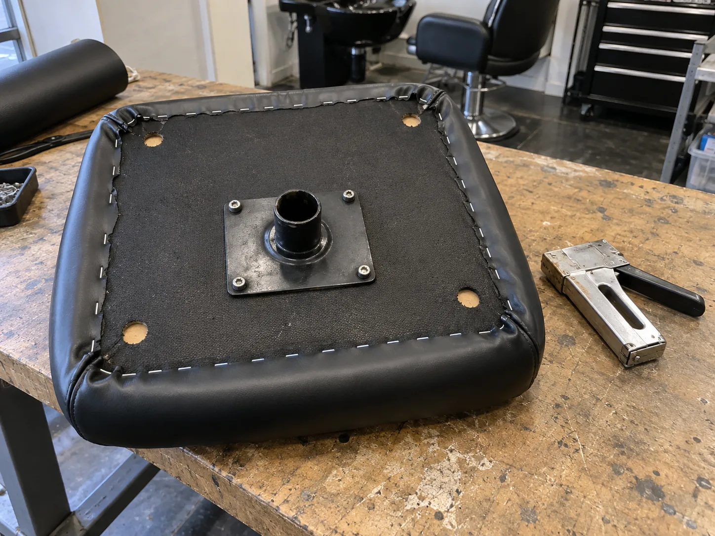 New black vinyl stapled to the underside of a styling chair seat