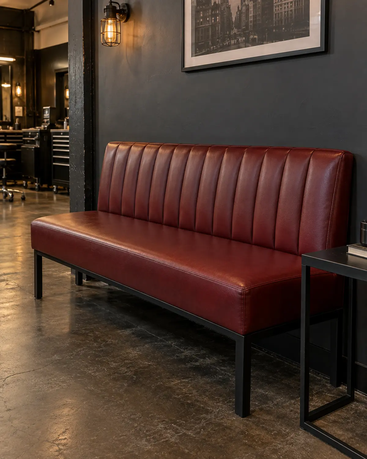 An oxblood channel-tufted waiting bench against a dark wall