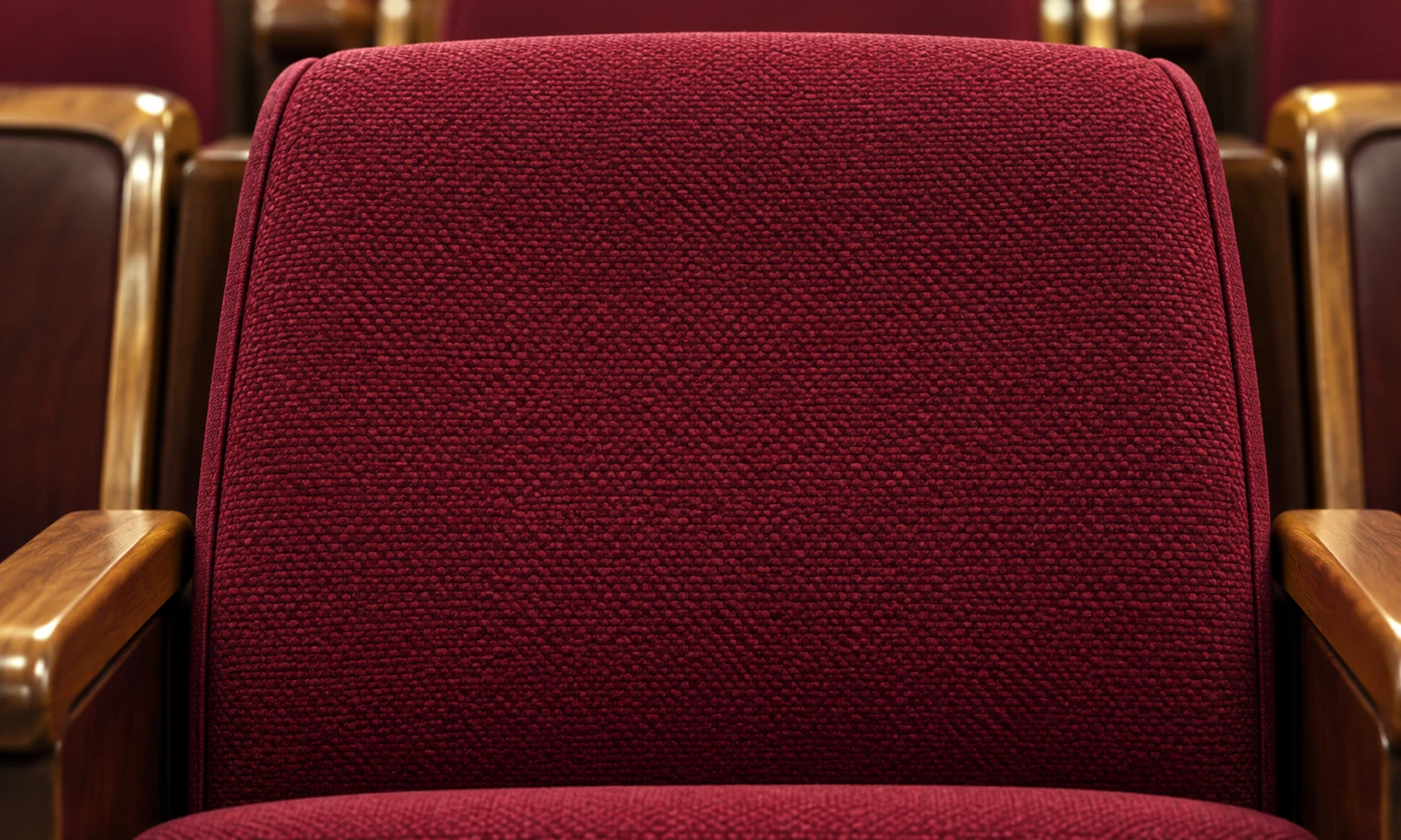 Close view of a burgundy woven backrest panel on a theater seat between wood arms