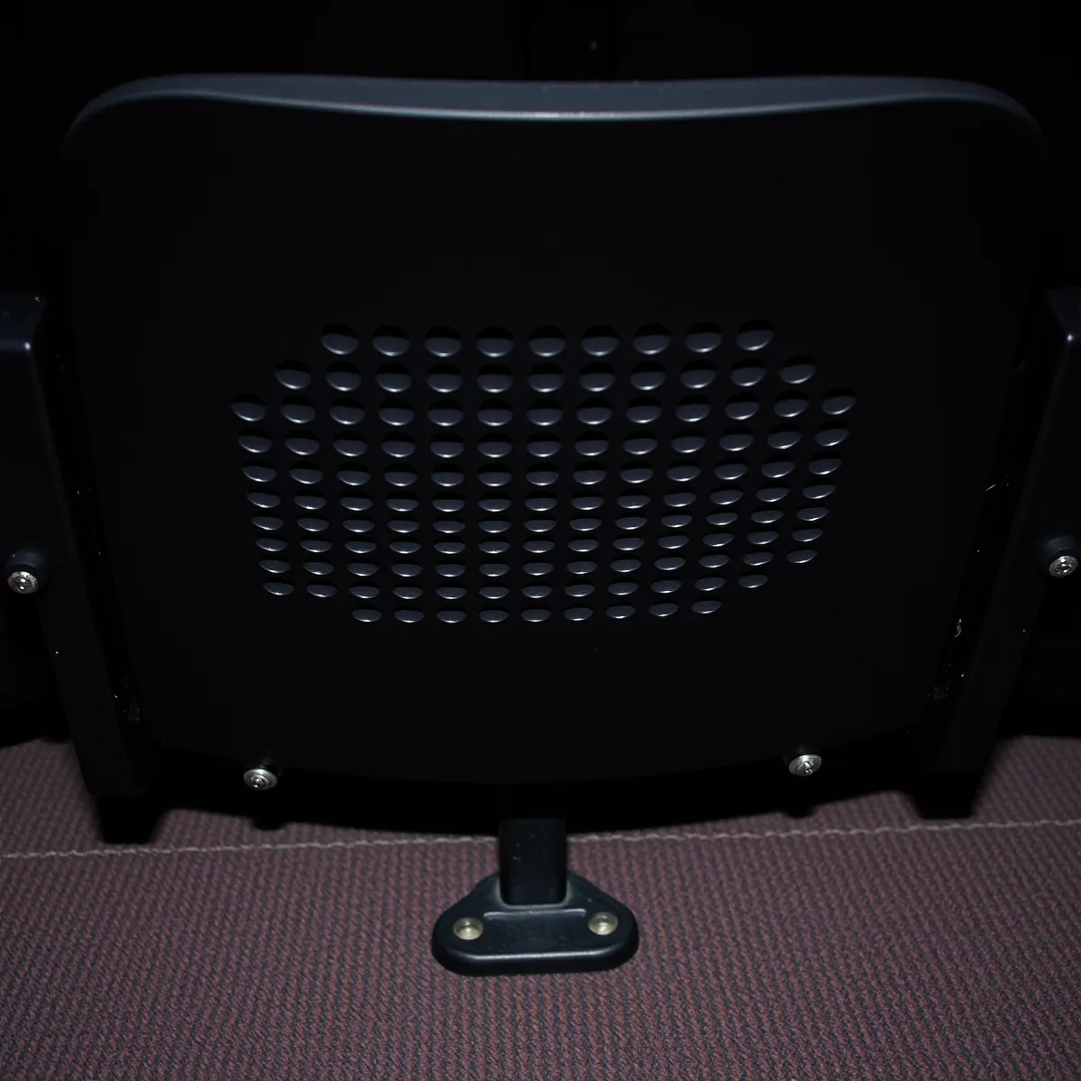 Perforated black outer back panel of a fixed auditorium seat on a standard bolted to the floor