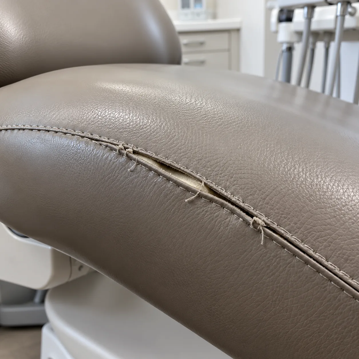 A torn, open seam on the taupe cushion of a dental chair