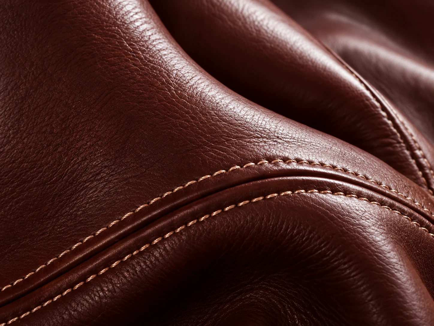 Contrast stitching along a curved seam on oxblood leather