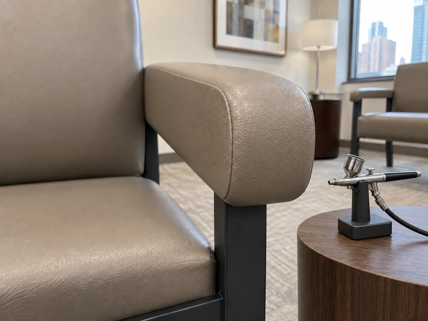 An airbrush on a small stand beside a freshly recolored taupe waiting chair arm