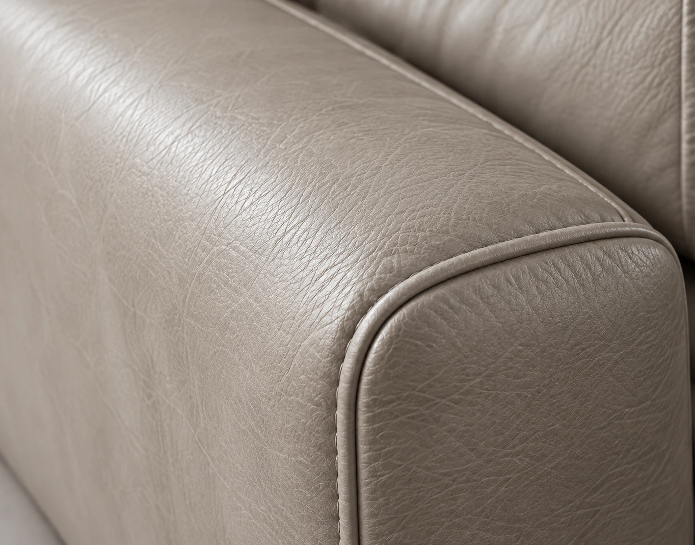 Macro view of a pale greige leather arm with a piped edge running down the front corner