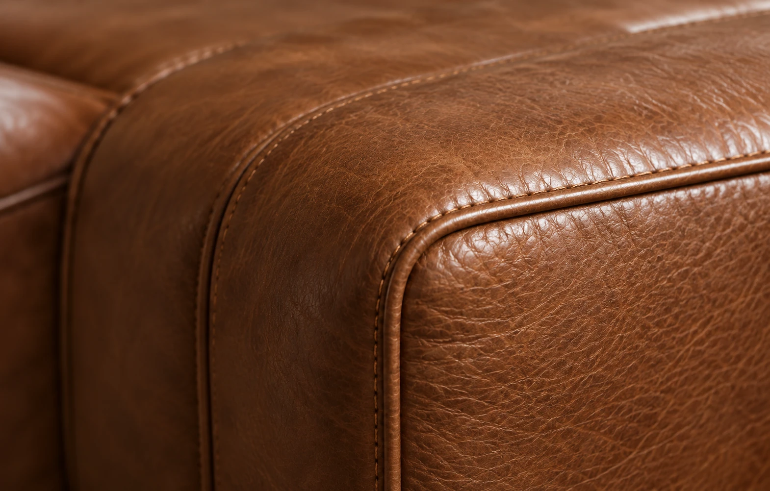 Macro view of the corner of a cognac leather sofa arm showing double topstitching and a rolled welt