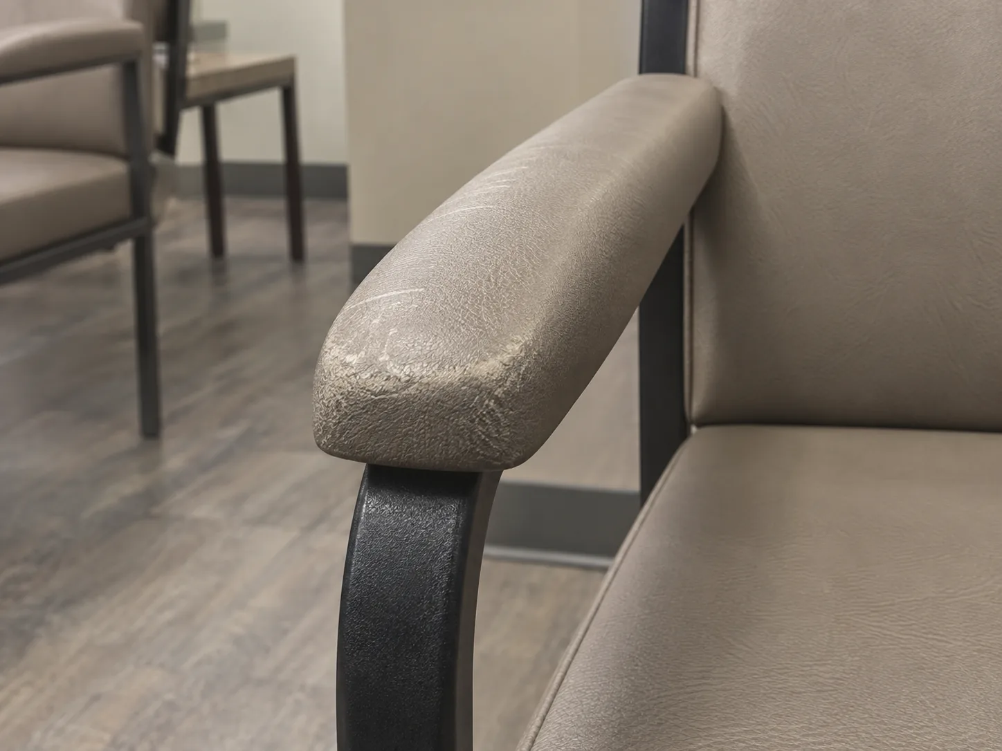 A worn, scuffed vinyl arm cap on a waiting room chair