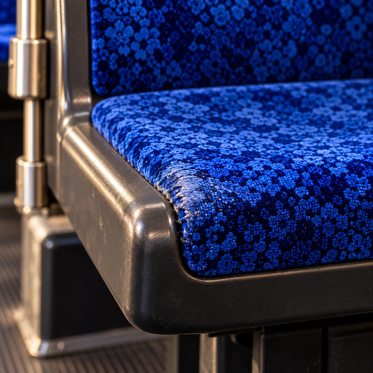 The worn, shiny aisle corner of a bus seat