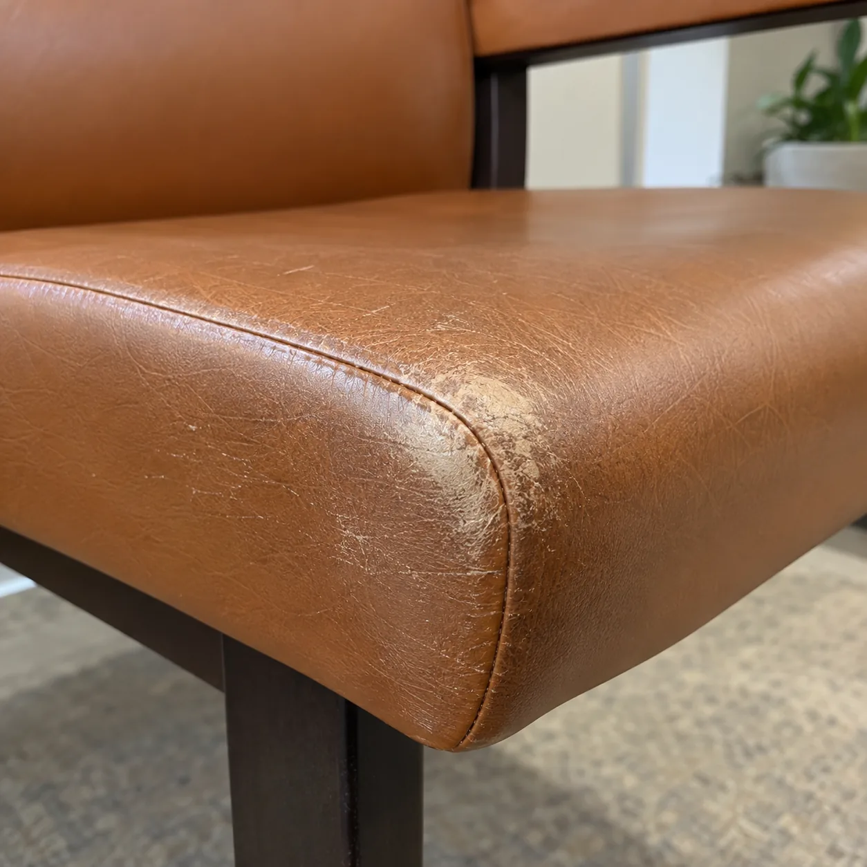 A worn, scuffed front corner on a cognac waiting room chair seat