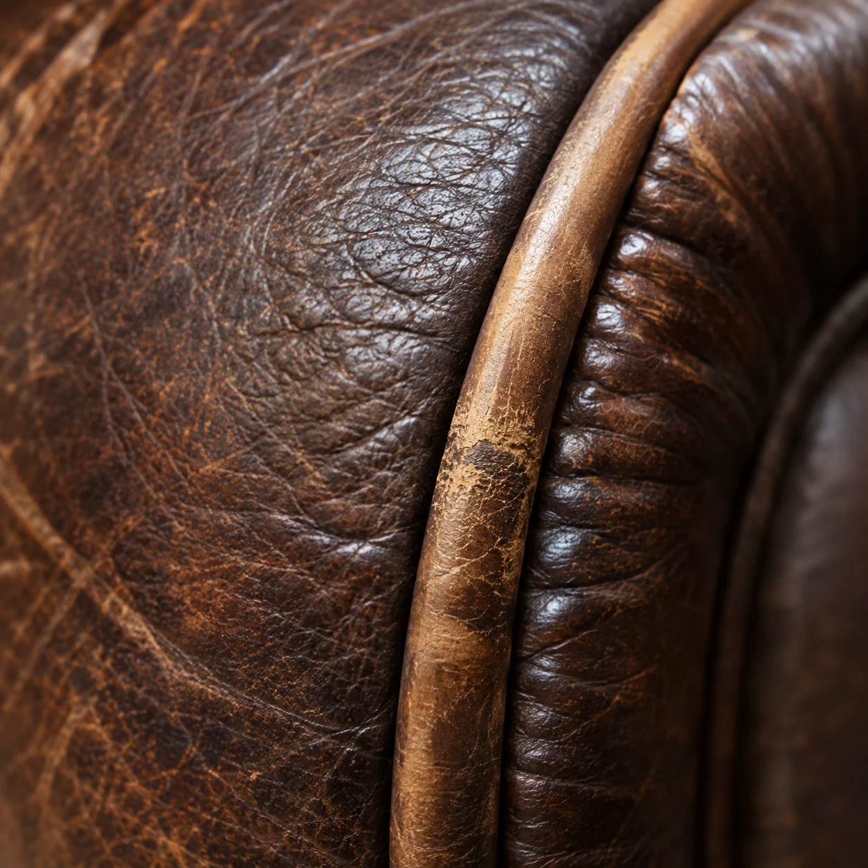 Worn welt piping along the roll of an antique leather sofa arm